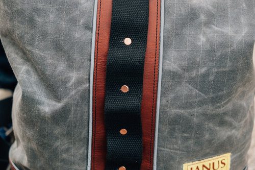 Close-up of a grey jacket with a brown leather strap and snaps.