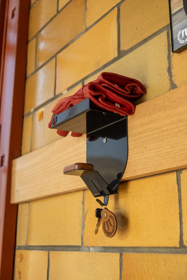Red scarf and keys hanging on a modern black wall hook against a brick wall.