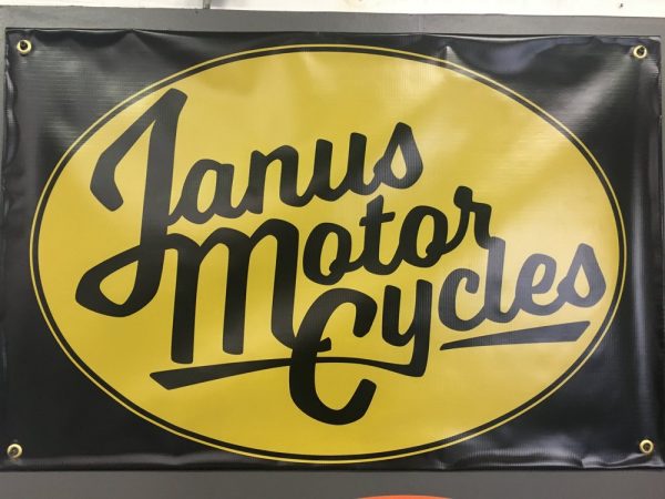 Janus Motorcycles banner with cursive logo on yellow and black background.