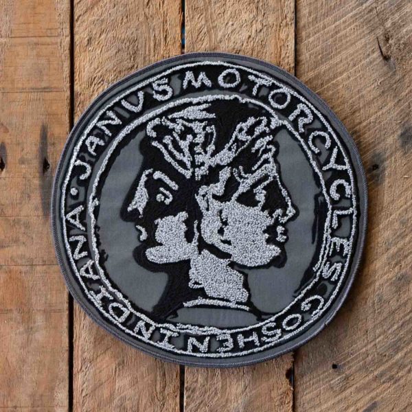 Embroidered motorcycle club patch with two-faced Roman god design on wooden background.