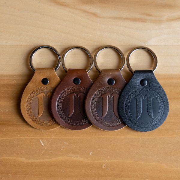 Four leather keychains with embossed designs on a wooden surface.