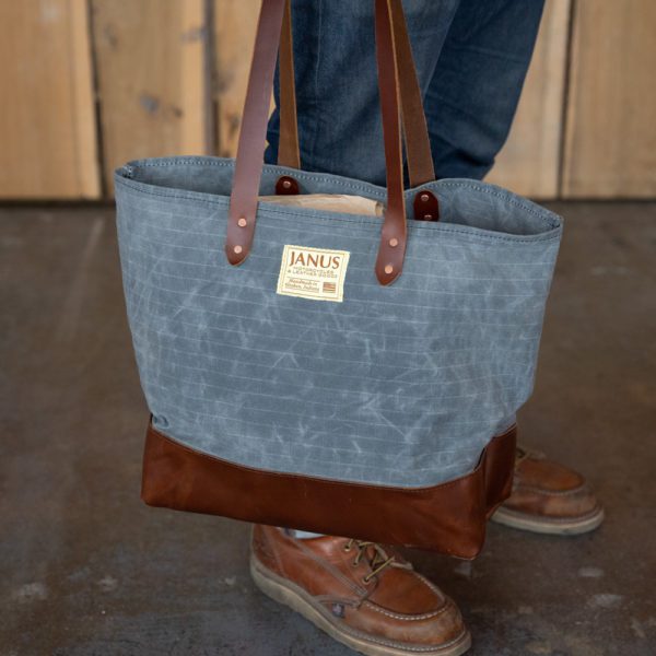 Person holding a stylish canvas tote bag with leather straps.