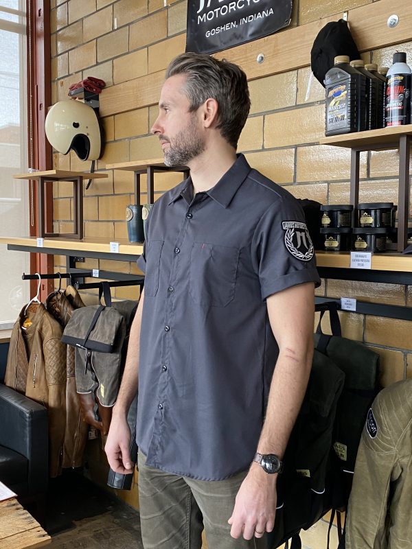 Man in a motorcycle shop wearing a casual shirt, with helmets and gear on display.