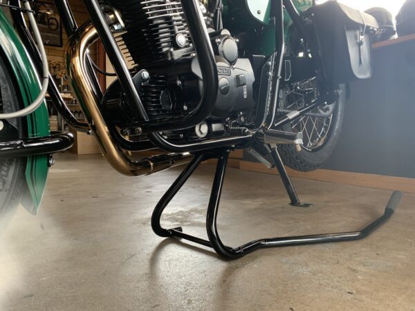 Close-up of a motorcycle's engine and chromed exhaust on a center stand in a garage.