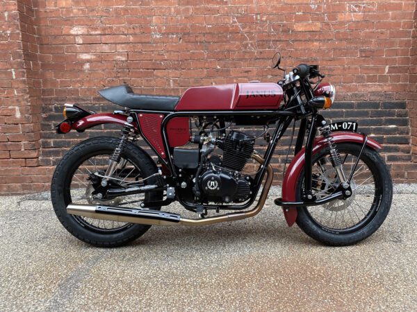 Classic red and black Janus motorcycle parked in front of a brick wall.