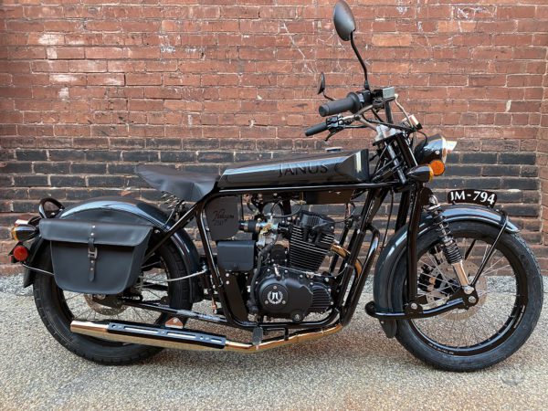 Black Janus motorcycle parked in front of a brick wall.