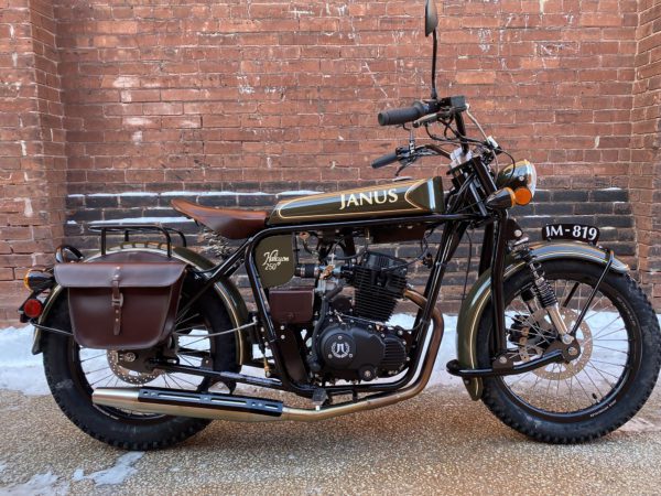 Classic motorcycle with side bag parked against brick wall.