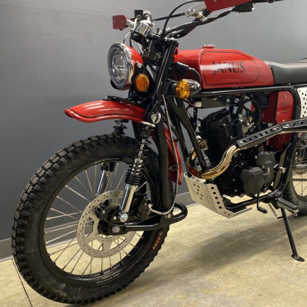 Red Janus Halcyon 250 motorcycle with knobby tires parked indoors.