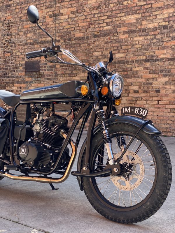 Black retro motorcycle parked against brick wall.