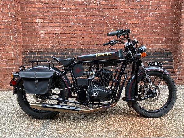 Vintage-style JANUS motorcycle parked against a brick wall.