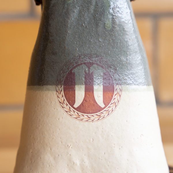 Close-up of a ceramic bottle with a logo and two-tone glaze.