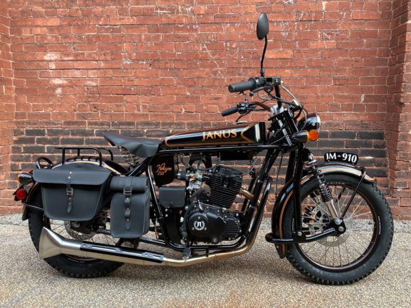 Classic black Janus motorcycle parked in front of a brick wall.