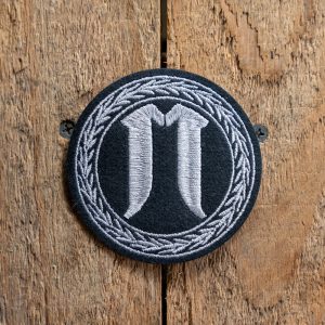 Embroidered monogram coaster with initials on wooden background.