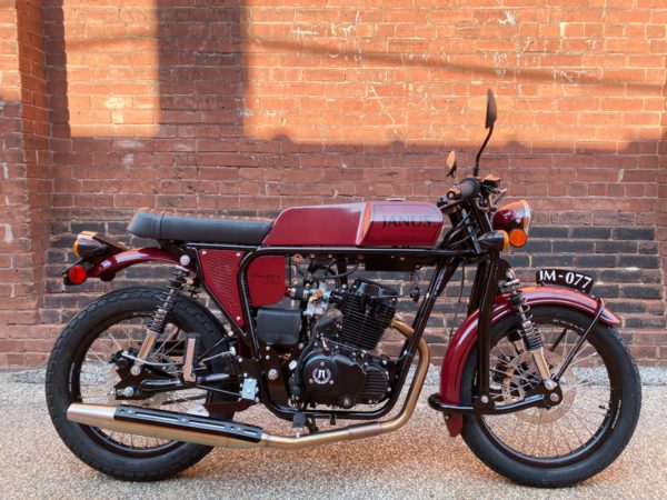 Vintage-style Janus motorcycle parked in front of a brick wall.