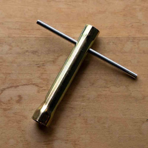 Brass T-shaped tuning fork on wooden surface.