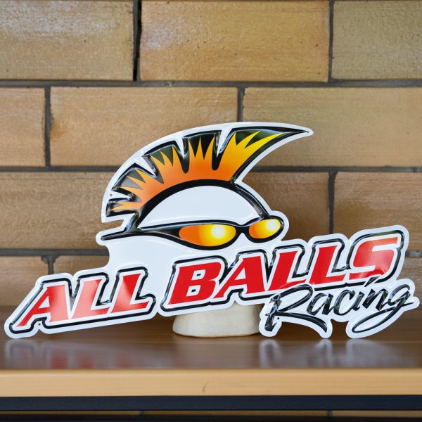 All Balls Racing logo with stylized sun and shades against a brick wall.