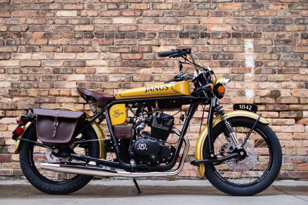 Classic yellow Janus Halcyon 250 motorcycle parked in front of a brick wall.