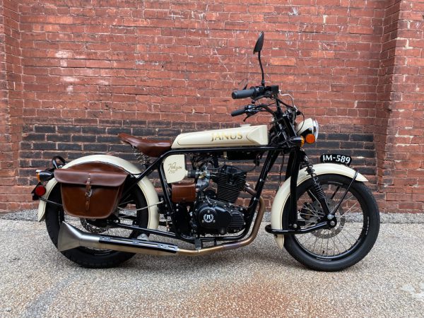 Classic tan Janus motorcycle with sidecar parked against a red brick wall.