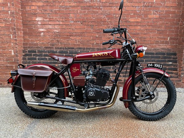 Vintage Janus motorcycle parked against a brick wall.