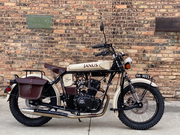 Vintage Janus motorcycle parked against a brick wall.