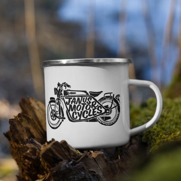 Enamel mug with Janus Motorcycles logo on a log in the forest.